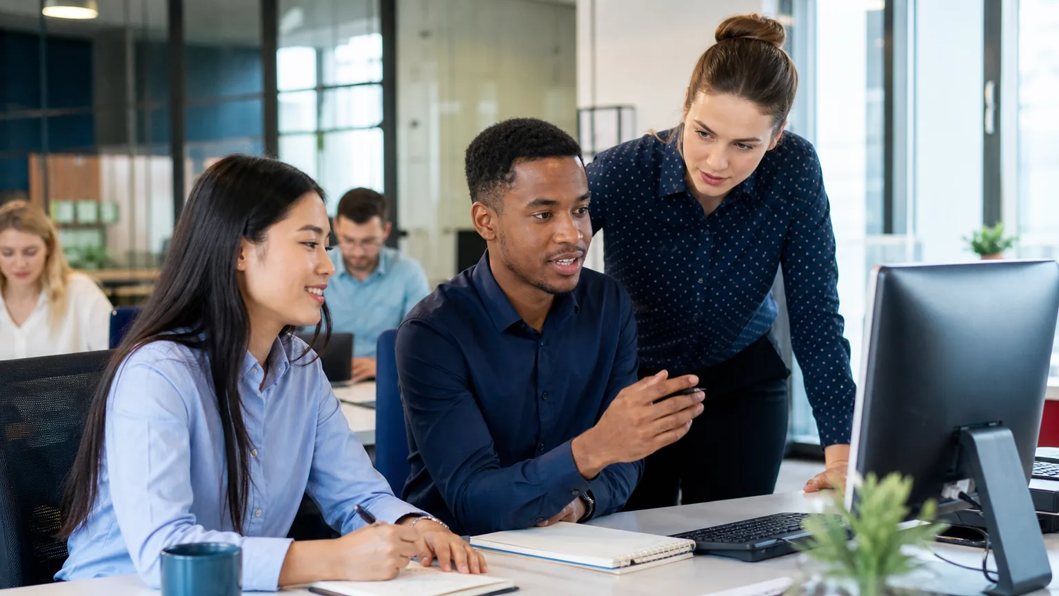 Entry-level office professionals collaborating at computers in a modern workplace